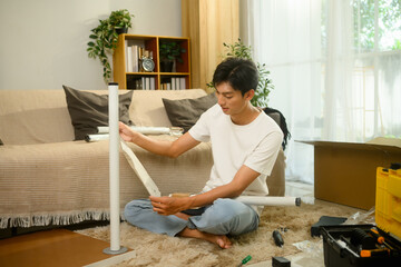 Young man reading an instruction manual while assembling furniture in a bright living room