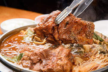 Lifting the pork bone of Korean-style gamjatang with tongs