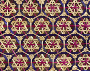 Close up of rattan art in geometrical hexagon and star shape pattern, in light brown, red, and purple color. Wicker art or rattan geometric weaving art. Seamless background texture.