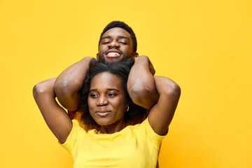 Fototapeta premium Happy African couple enjoying playful moments against a bright yellow background, showcasing vibrant emotions and casual summer style in matching yellow outfits