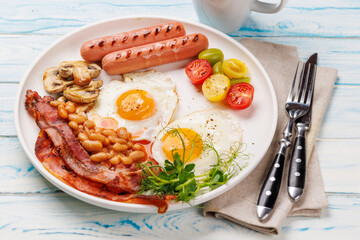 A classic breakfast plate featuring sunny-side-up eggs, crispy bacon, sausages, and fresh tomatoes