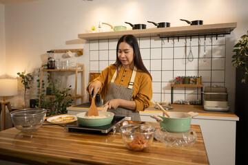Smiling woman in apron stirring food in frying pan on an induction stove