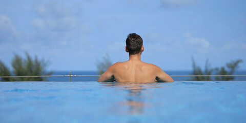 Tourist relaxing in infinity pool overlooking tropical ocean