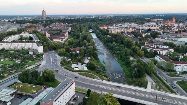 Panorama flight along river Wertach with trees during sunset and hotel tower in the background in Augsburg, Germany