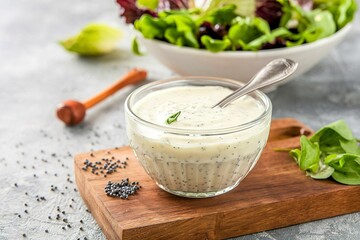Poppy seed salad dressing or sauce in a glass dish with green salad leaves in the background