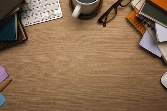 Top view of wooden desk with stacked books, a coffee cup, keyboard and glasses