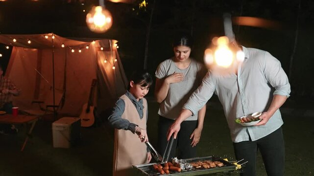 Family together camp in garden, Mom dad and daughter grill food for family member. Outdoor camping activity to relax with nature and spend time with young generation cross generation gap. Divergence.