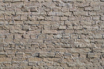A weathered brick wall showcases various shades of beige and brown, emphasizing the texture and unique patterns of laid masonry. Sunlight casts soft shadows on the surface