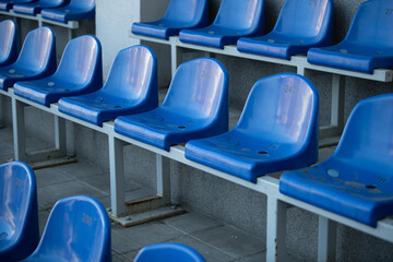 Fototapeta premium Rows of blue plastic seats are arranged in a stadium, stark and empty, ready for fans to fill them during an exciting outdoor sporting event later in the day