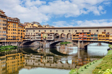 The Ponte Vecchio bridge in Florence showcases its colorful buildings and shops reflecting in the tranquil waters Arno river.