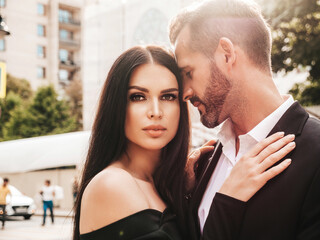 Beautiful fashion woman and her handsome elegant boyfriend in suit. Sexy brunette model in black evening dress. Fashionable couple posing in the street in Europe. Brutal man and his female outdoors