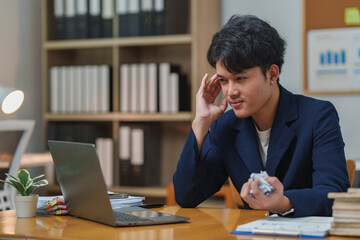 Fototapeta premium Young professional attentively participating in an online meeting, seated at a desk with a laptop. Office supplies and a small plant create a productive workspace ambiance