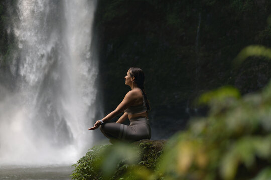 Woman practising yoga in front of waterfall on the island of Bali