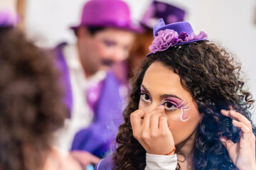 Fototapeta premium Young woman applying elaborate stage makeup, wearing a purple hat and costume, preparing for a theatrical performance