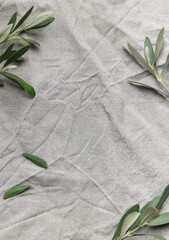 Olive branches framing wrinkled gray linen cloth background