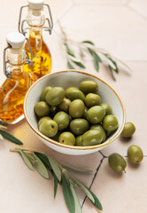 Green olives in bowl with olive oil bottles and olive branches on tiled table