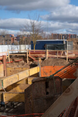 urban construction site with exposed earth and structural beams, featuring construction materials, industrial machinery, and urban skyline under a cloudy blue sky backdrop. urbanization, framework
