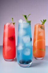 vibrant trio of icy refreshing cocktails garnished with fresh mint, showcasing bright red, blue, and orange colors against a soft pastel background, pleasing, frozen, cooling, hydration, thirsty