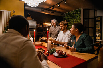 A White man in his 30s, presenting fresh bread to his family and his mid-30s Black wife, as they sit together around a wooden table in a cozy kitchen, and his elderly White mother stands beside them