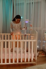 A White mother in her early 30s, smiling as she talks to her infant baby while standing over its...