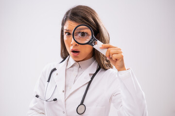 Studio shot portrait of worried female doctor who is looking through magnifying glass.