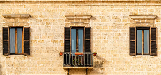old yellow facade of house with three brown vintage wooden windows in retro italian european style