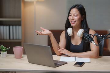 Smiling podcaster speaking into microphone and gesturing while recording audio podcast at home...