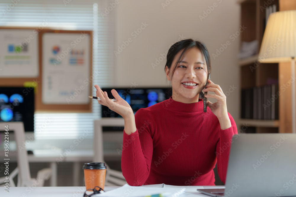 Aufkleber young manager is making a business call and holding a pen while working at her desk in a modern offi