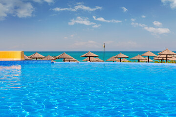 Luxury hotel pool in Sharjah with crystal-clear water, surrounded by elegant sun loungers. Stunning sea views and a golden sandy beach create a relaxing atmosphere under the bright daytime sun.