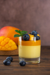 Mango panna cotta mousse pudding with blueberries and mint leaf on a brown wooden table. Vegan...