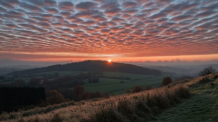 Dramatic Sunset Over Hilly Landscape with Orange Sky Golden Sunlight and Silhouetted Hills in Rural Scene