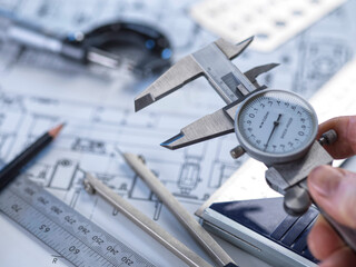 Close-up of a hand using calipers on a technical drawing for engineering measurement and quality control