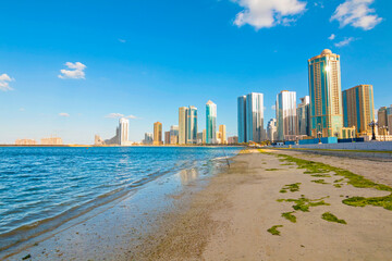 Sharjah city skyline at sunrise with golden light reflecting on modern skyscrapers. Serene beach...