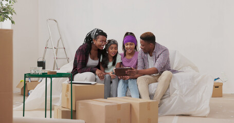 A happy family of African American descent sits on the couch in their apartment during renovation....