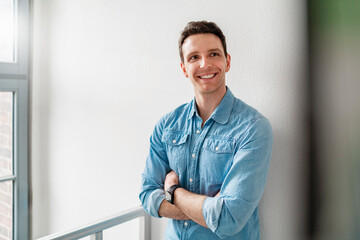 Young man in a denim shirt smiling confidently in an office setting