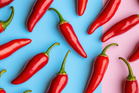 Vibrant red chili peppers arranged on a colorful blue and pink background. - Powered by Adobe