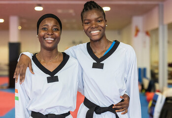 Two women in a judo school in Madrid smiling and wearing taekwondo uniforms
