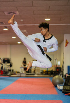 Martial artist performing a high kick in a dojo wearing a judo uniform and black belt