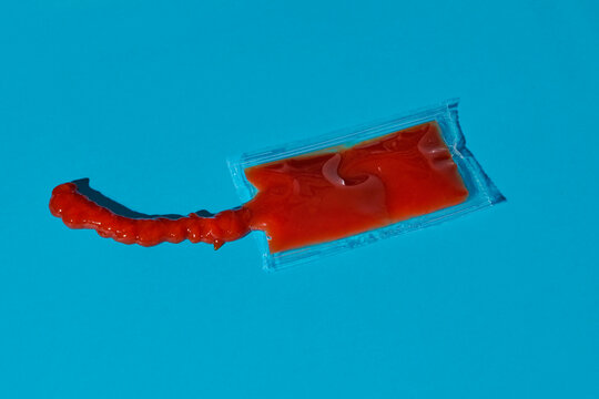 Open ketchup packet with contents squeezed out on a blue background