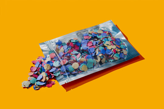 Colorful confetti spilling from a plastic bag with a press-to-seal zipper on an orange background