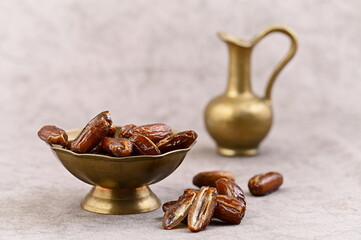 Dates in a brass bowl and a small teapot, neutral background, still life.