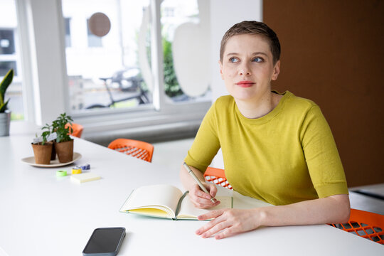 Woman in green shirt writing in notebook at office desk