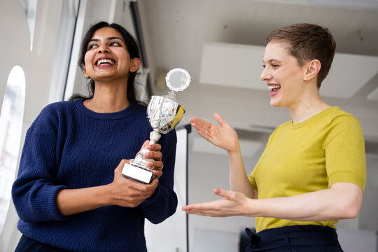 Two women celebrating a victory with a trophy in an office setting