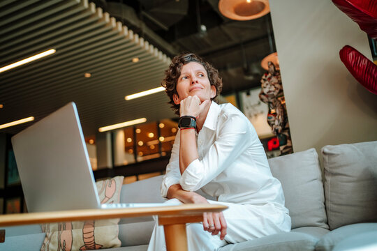 Thoughtful businesswoman sitting with hand on chin by laptop in hotel lobby