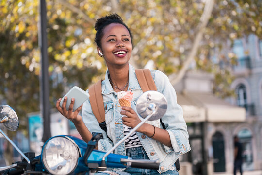 Smiling young woman sitting on a scooter eatu�ng ice cream