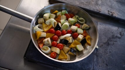 Diced vegetables jumping in a professional stainless steel pan, handled by a chef in a restaurant kitchen