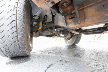 Undercarriage view of 1996  classic American 4x4 pickup truck SUV showing rusty frame, suspension, axle, driveshaft, and exhaust system  © Hrach