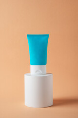 Plastic blue tube for cream or lotion. Skin care or sunscreen cosmetic with stylish props on cream background.