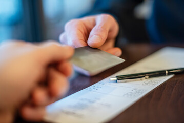 Close-up of hands exchanging a credit card over an invoice in a business setting
