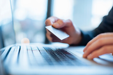 Hand holding a credit card over a laptop for online payment